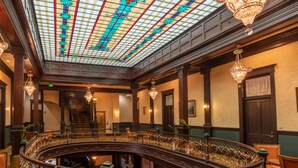 A grand interior with a glass ceiling, ornate railings, and chandeliers. - Geiser Grand Hotel (Baker City)