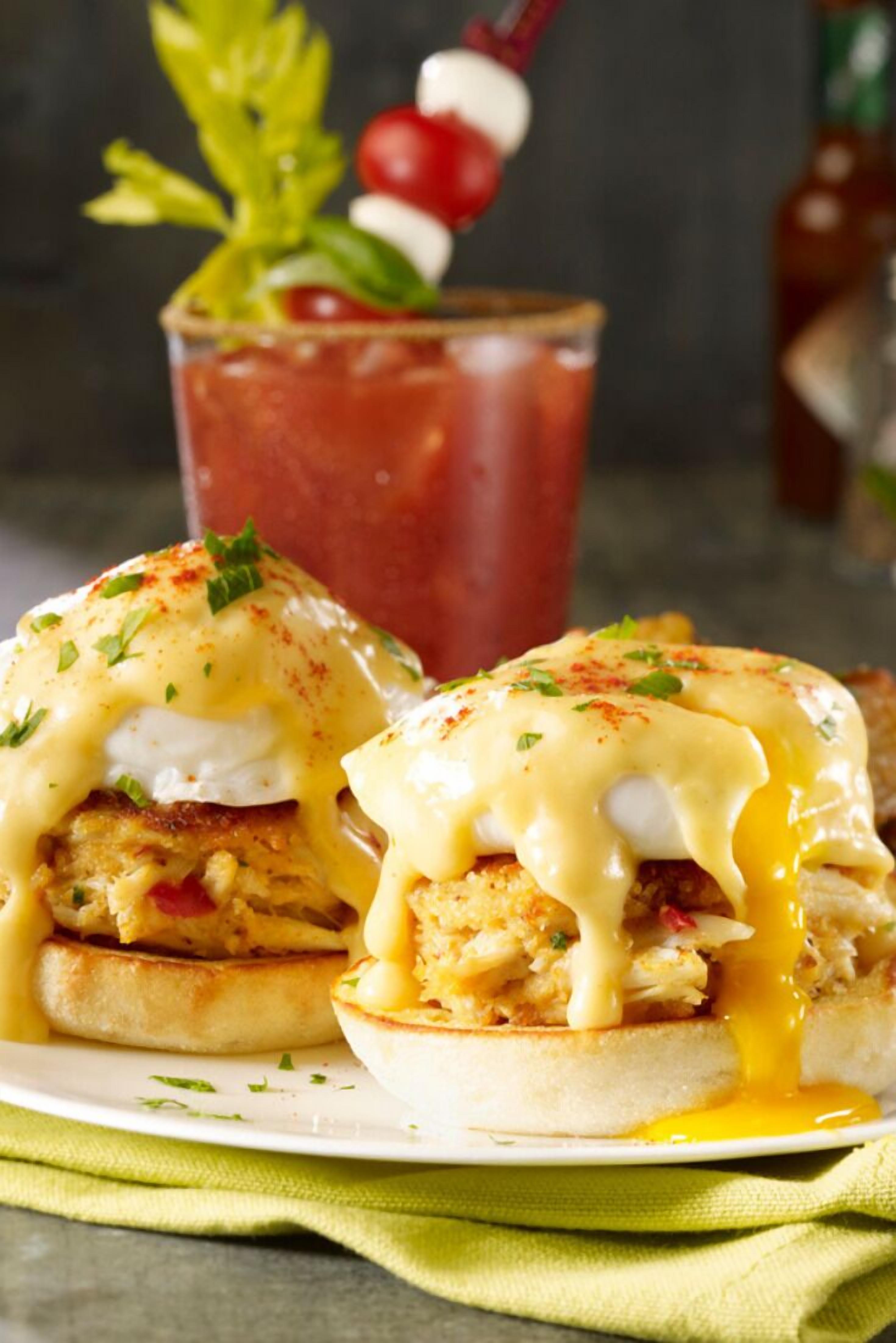 A plate of eggs Benedict with hollandaise sauce, garnished with herbs, and a cocktail glass in the background.