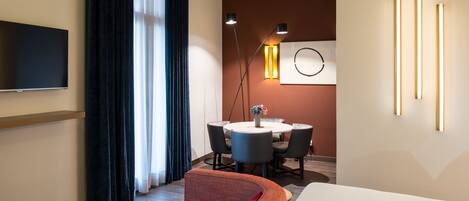 Een moderne hotelkamer met een flatscreen televisie, een bank, een eettafel met stoelen en een vloerlamp.