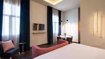 Una habitación de hotel moderna con una cama grande, un escritorio con silla, una mesita y un televisor montado en la pared.