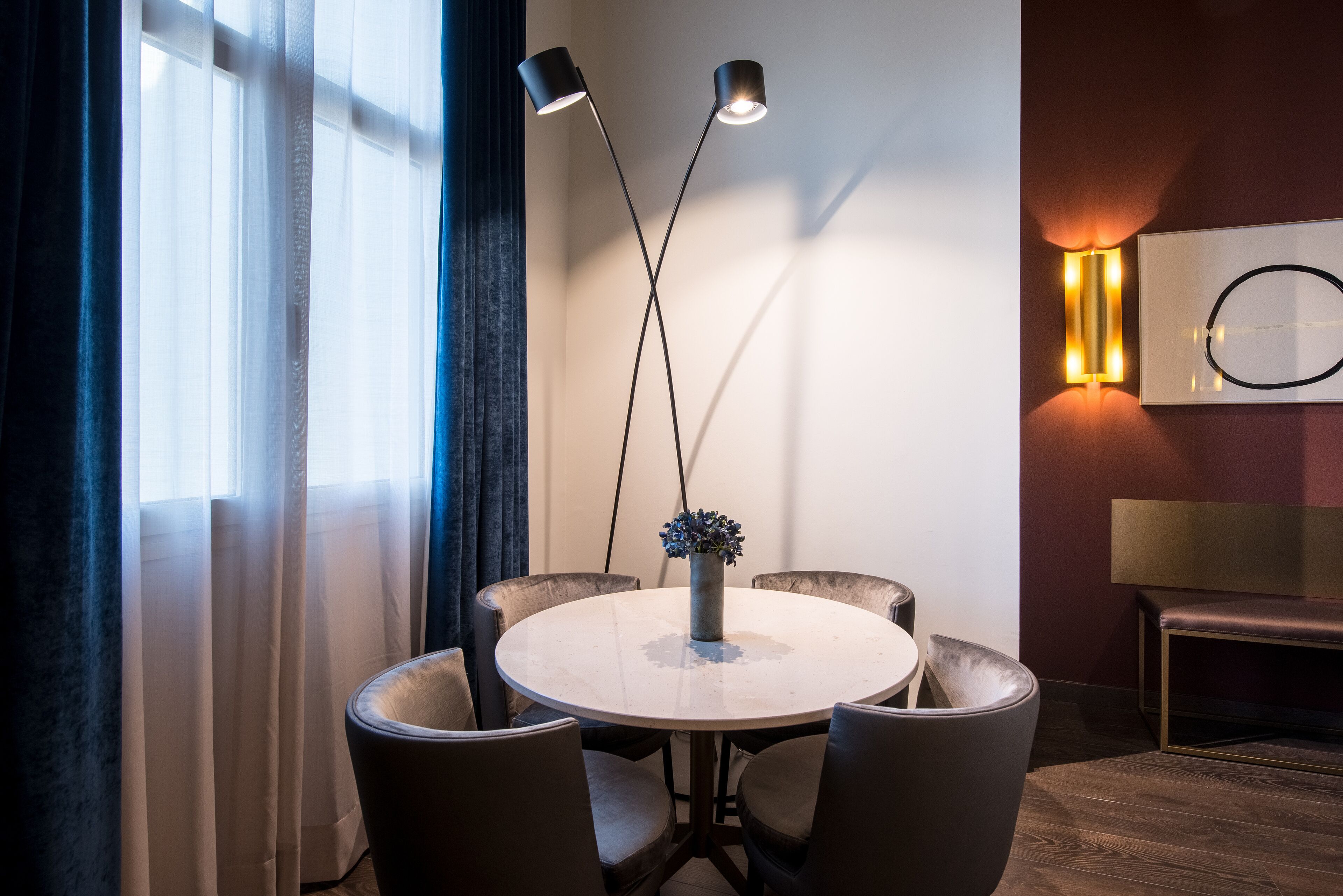 Una mesa redonda con seis sillas, dos lámparas de pie, un florero con flores y una lámpara de pared.