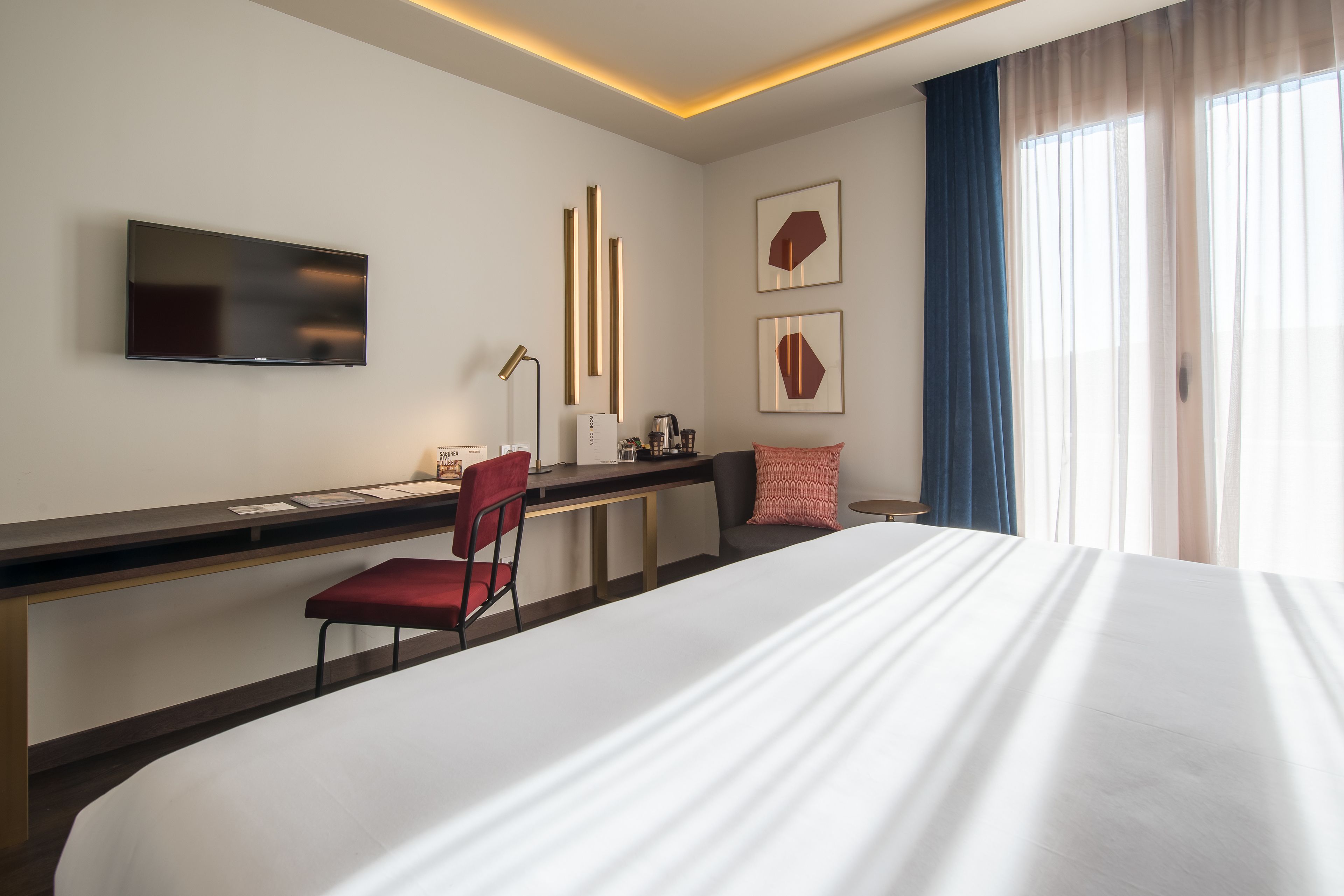 Habitación de hotel con cama, escritorio con silla, televisor de pantalla plana y una obra de arte en la pared.