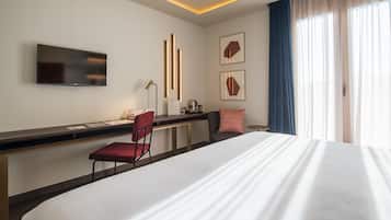Habitación de hotel con cama, escritorio con silla, televisor de pantalla plana y una obra de arte en la pared.