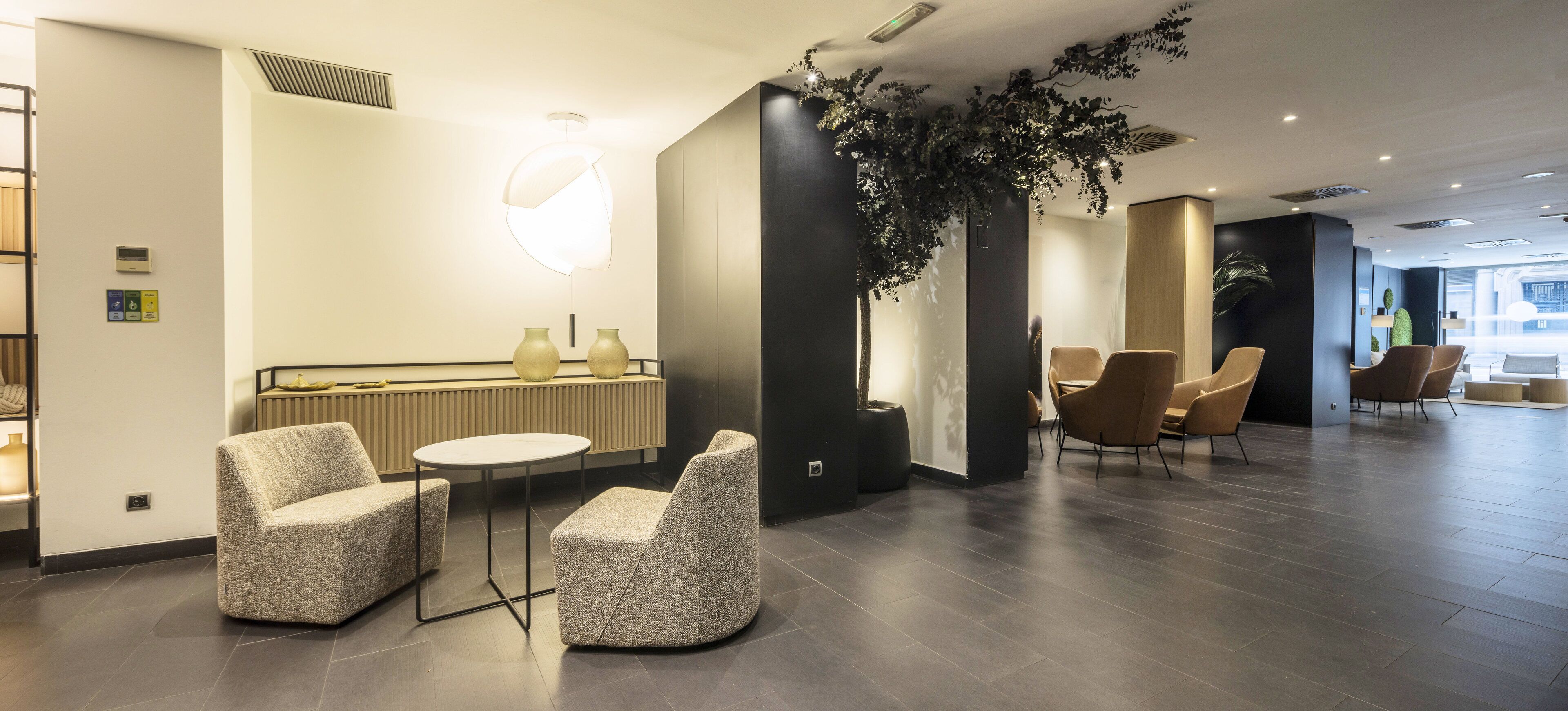 En modern hotellobby med en receptionsdisk, en sittgrupp och en stor växt.