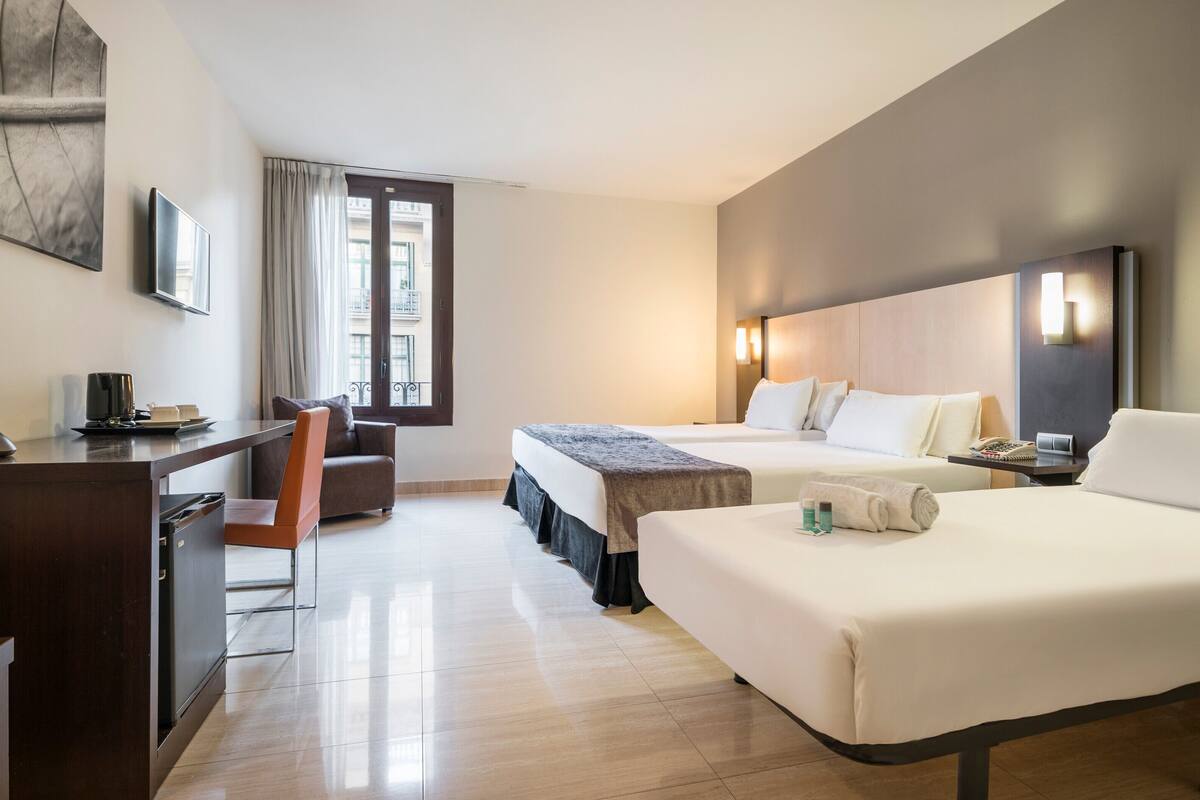 A hotel room with two beds, a desk with a computer, a chair, and a window with curtains.
