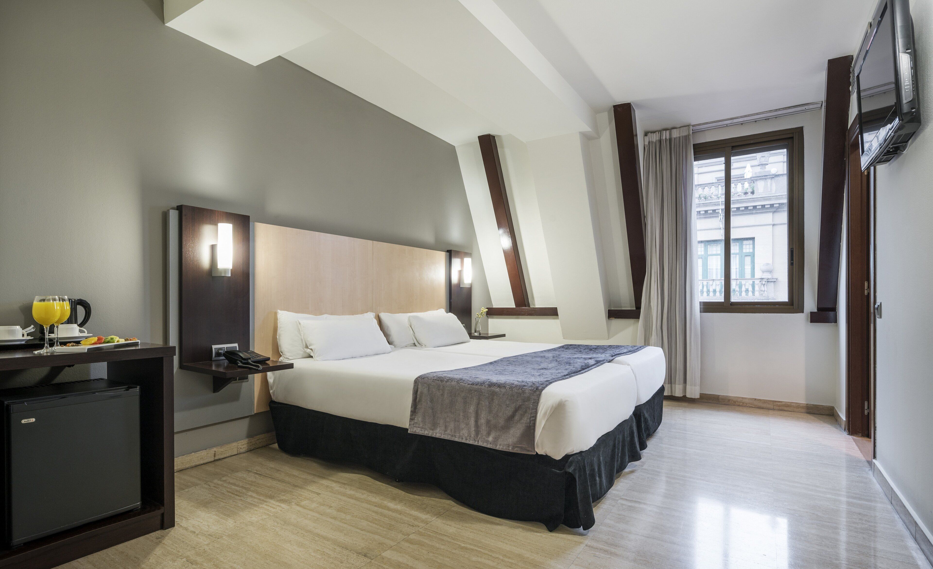 Una habitación de hotel con cama, mesita de noche y un escritorio pequeño con refrigerador.