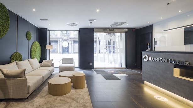 Un hall d’hôtel moderne avec un comptoir d’accueil, un canapé et deux petites tables rondes.