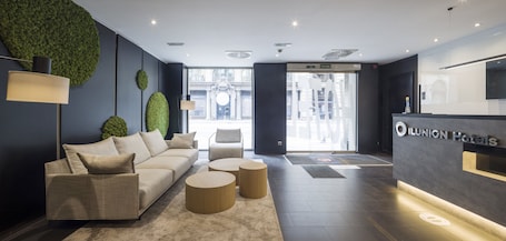 A modern hotel lobby with a reception desk, a sofa, and two round coffee tables.