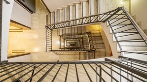 Un escalier en colimaçon avec une rampe en métal, des marches en marbre et un luminaire fixé au mur.