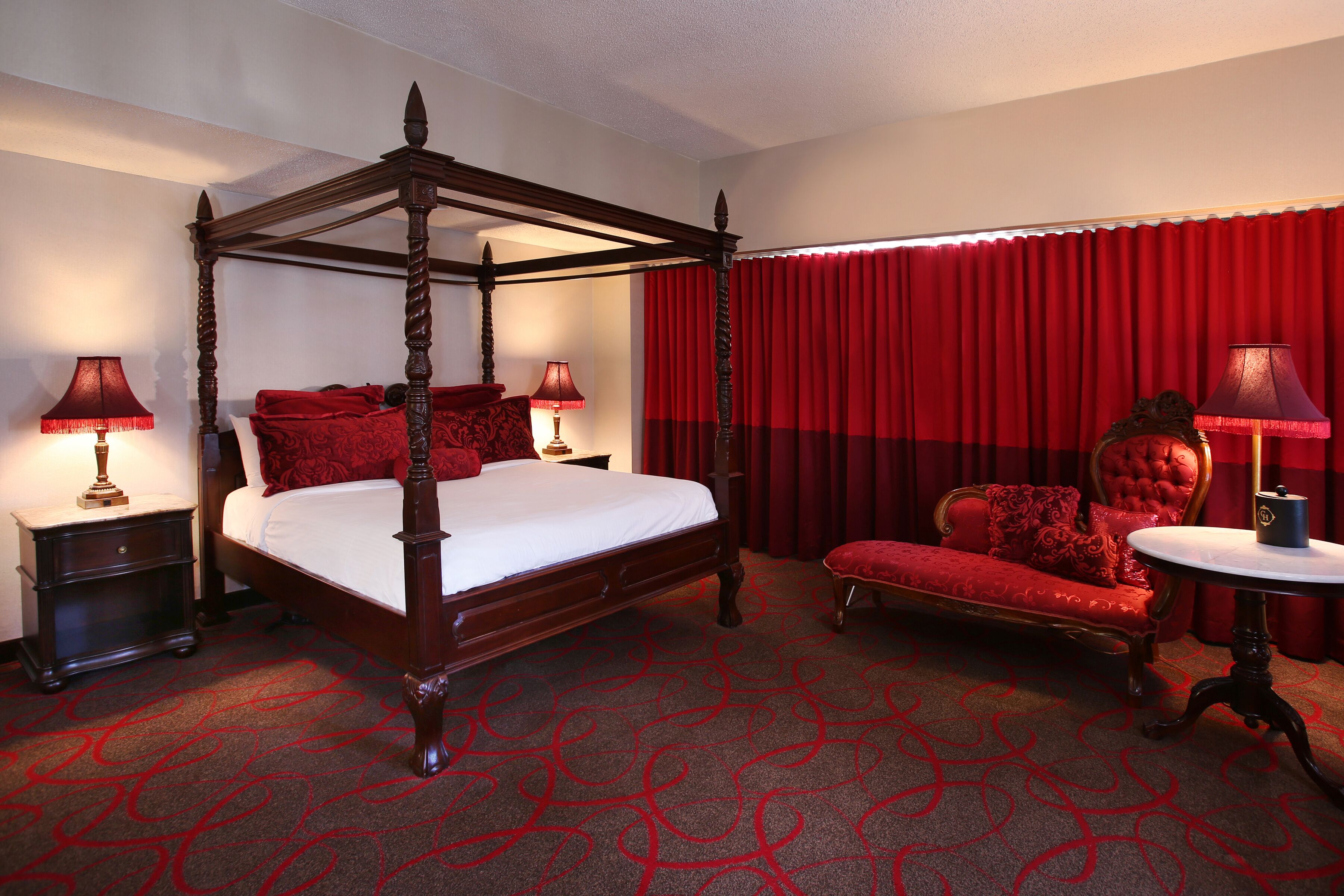 A four-poster bed with a red canopy, a red upholstered sofa, and a round table with a lamp.