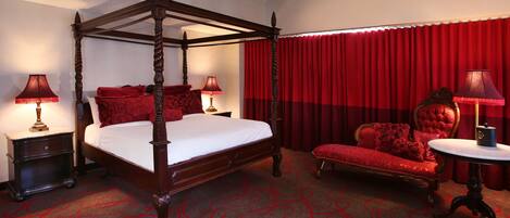 A four-poster bed with a red canopy, a red upholstered sofa, and a round table with a lamp.