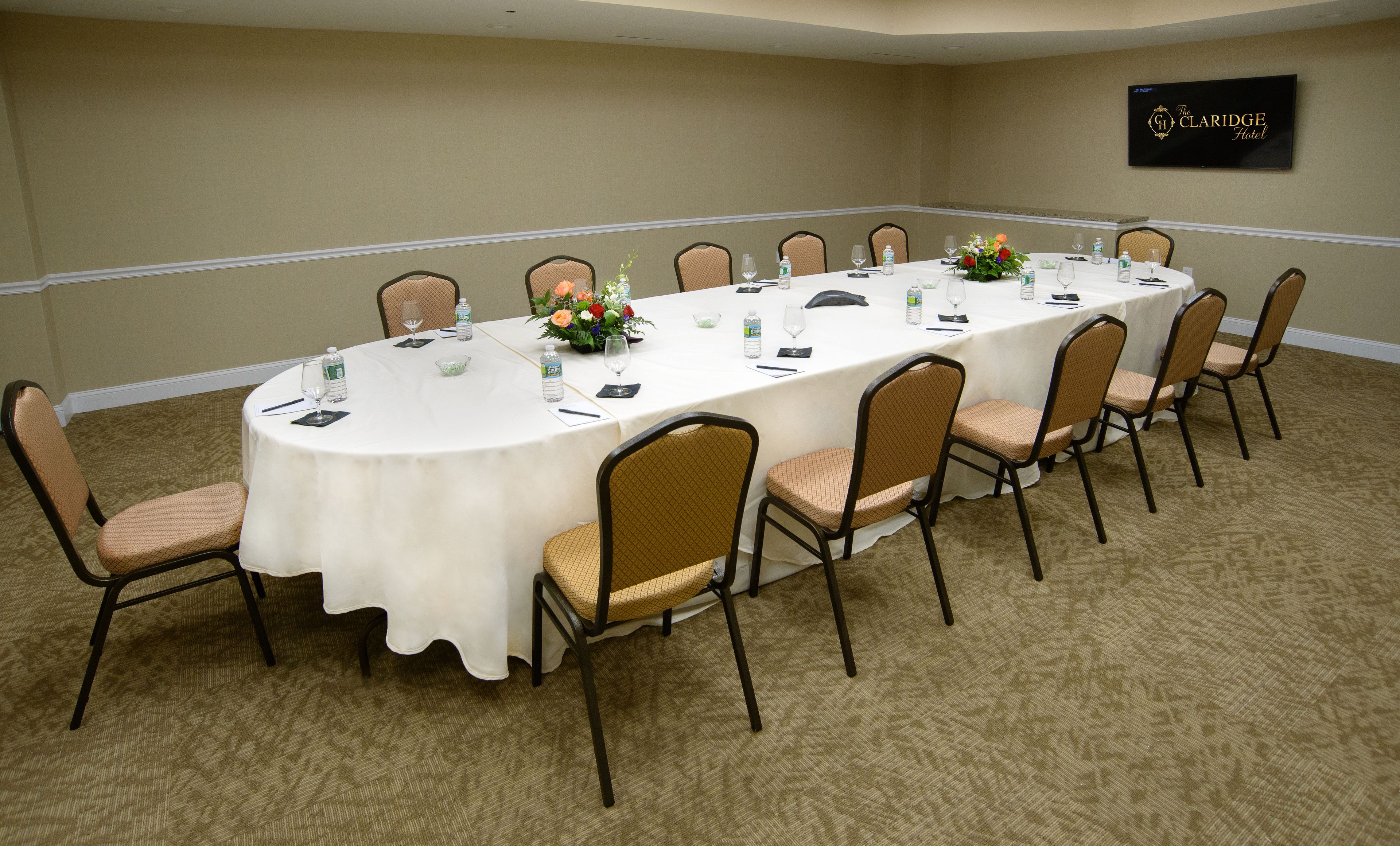 A conference room with a long table, chairs, water bottles, and a flower arrangement.