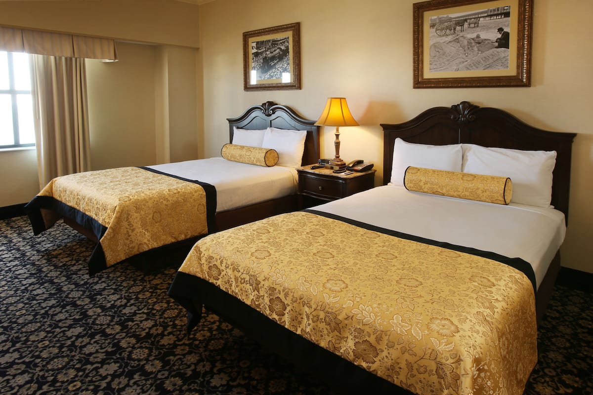 A hotel room with two beds, a nightstand with a lamp, and two framed pictures on the wall.
