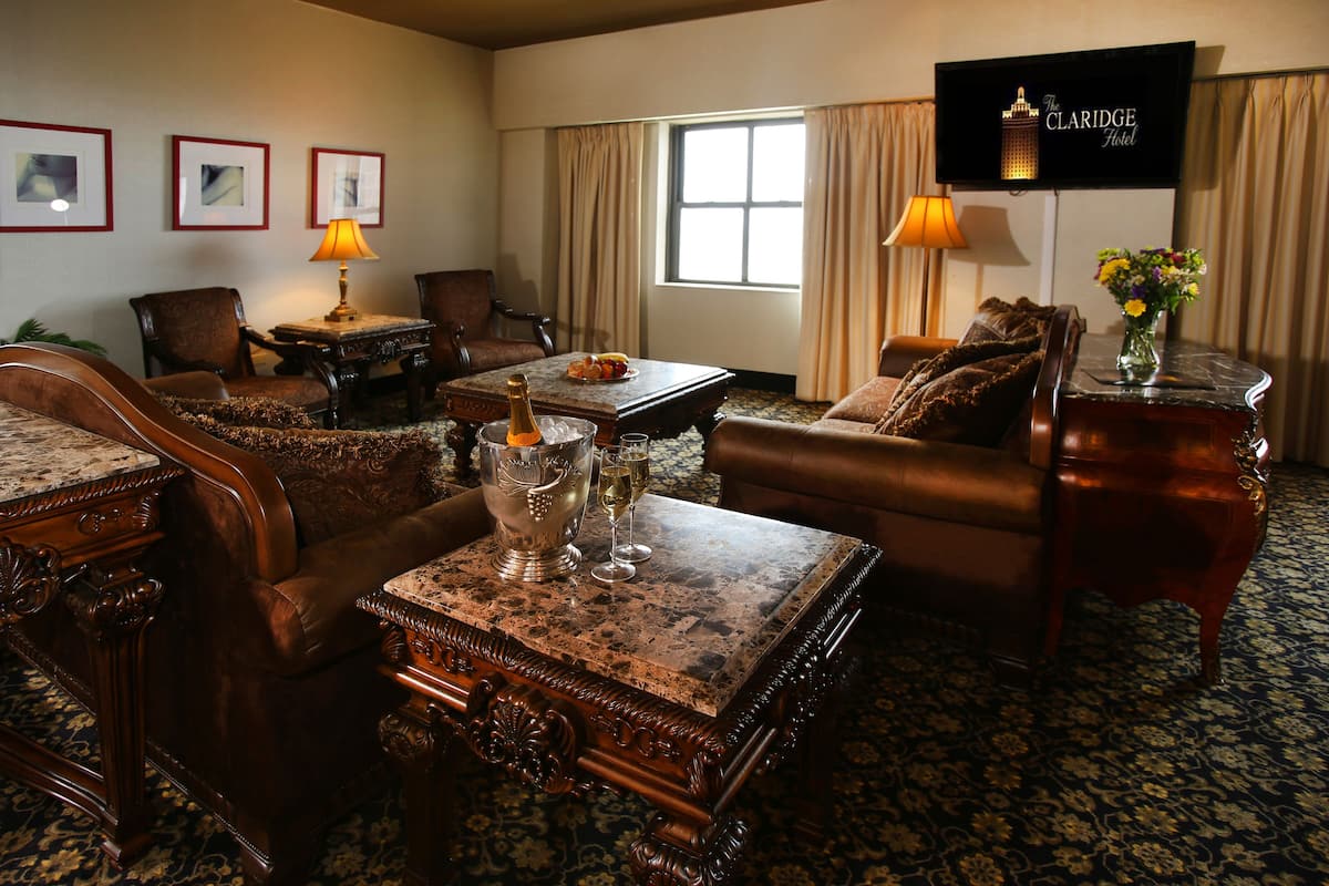 A hotel room with a large window, a television mounted on the wall, and a dining table with a bottle of champagne and glasses.
