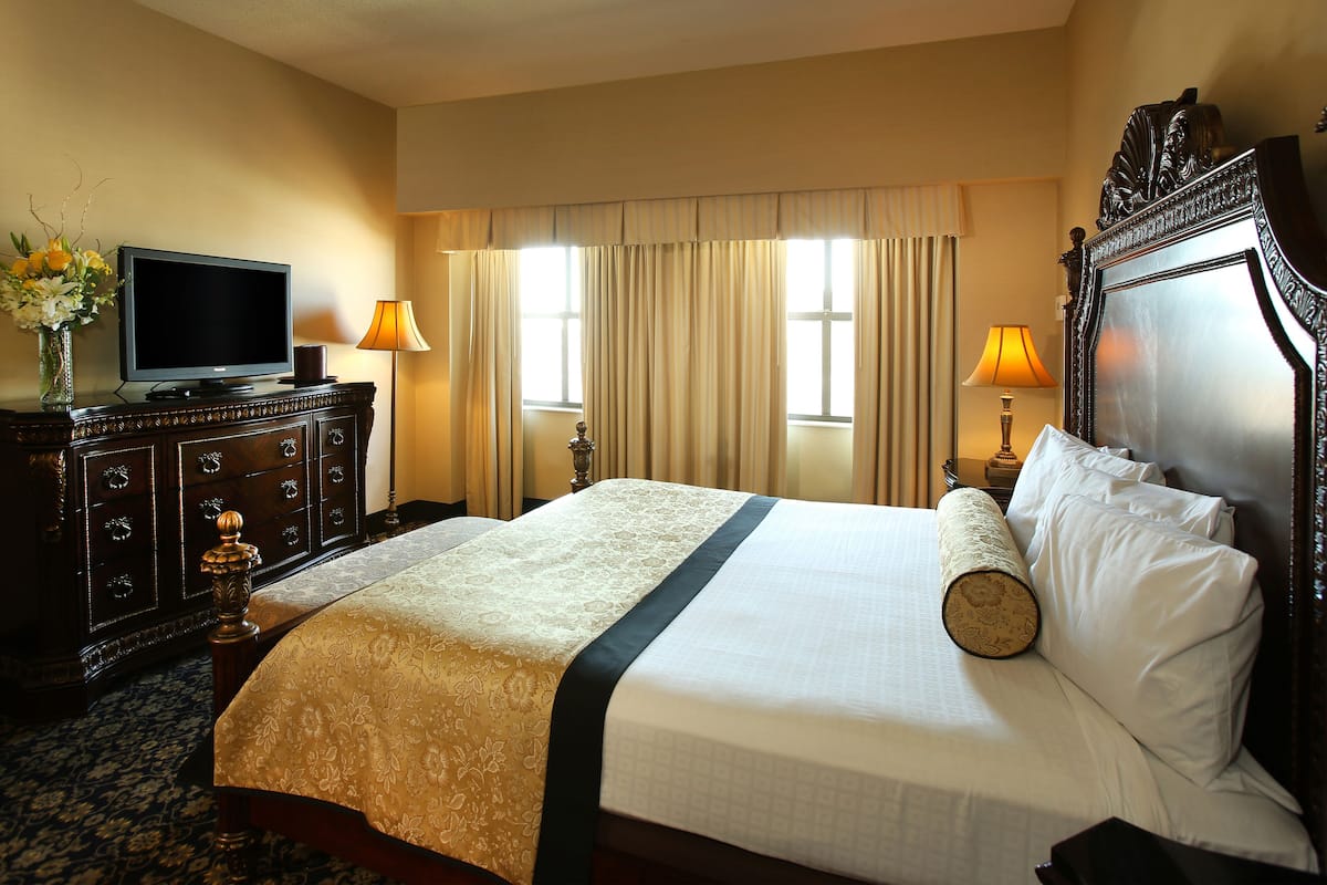 A hotel room with a bed, a dresser, a television, and two lamps.
