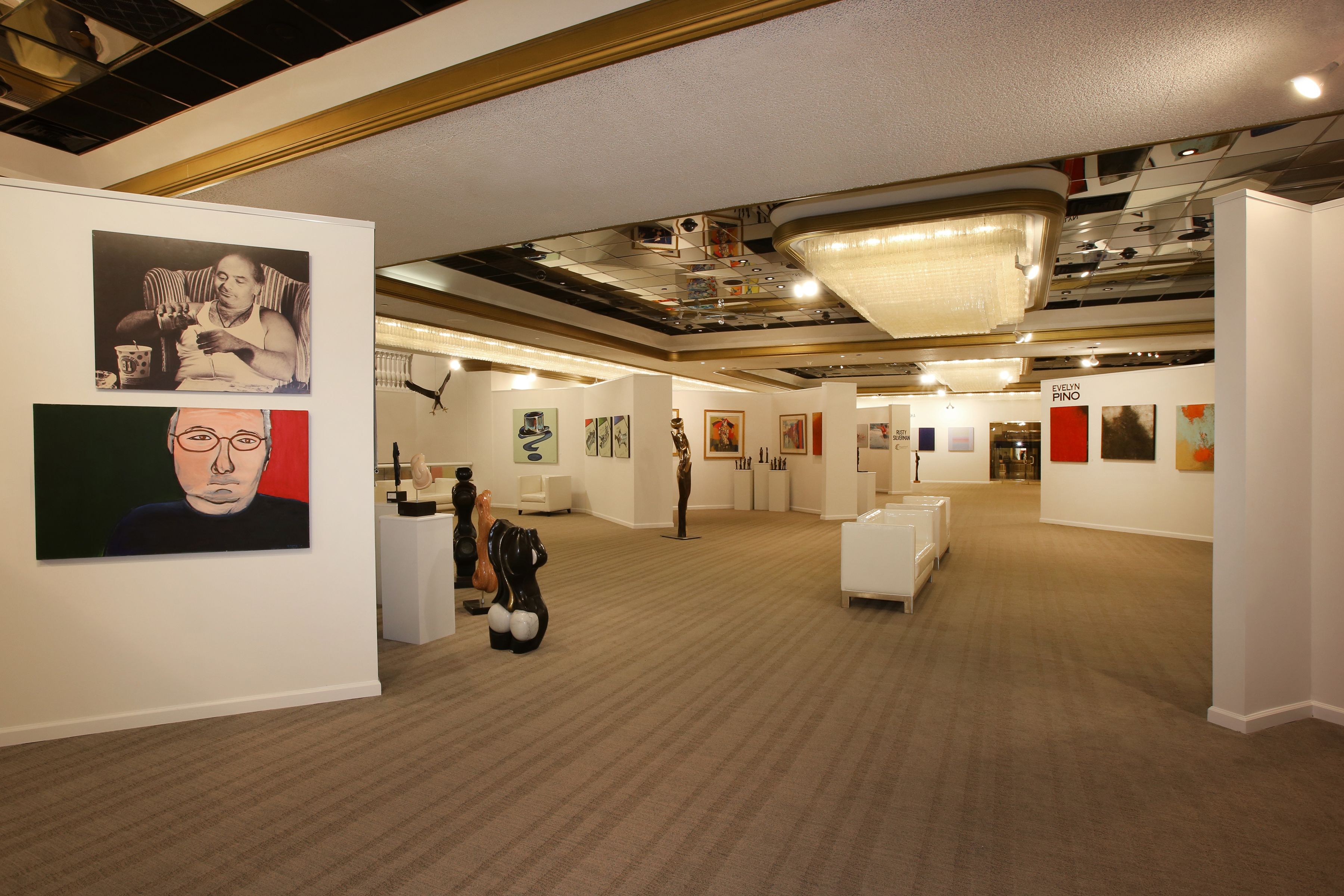 An art gallery with various artworks on display, a white reception desk, and a carpeted floor.