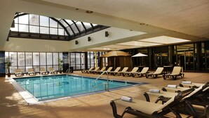 An indoor swimming pool with lounge chairs and umbrellas, large windows, and a high ceiling. - The Claridge Hotel (Atlantic City)