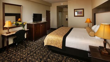 A hotel room with a large bed, a desk with a chair, a television, and a mirror.
