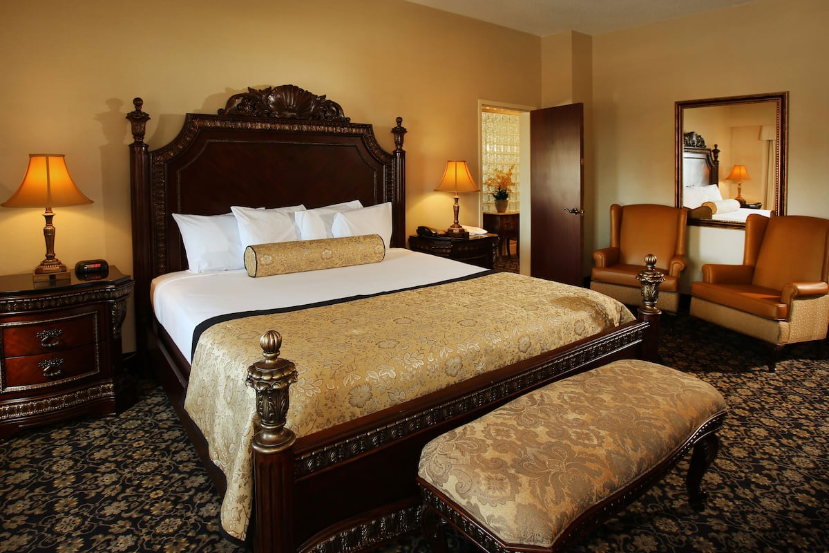 A hotel room with a large bed, two bedside tables, a chair, a bench, and a mirror.
