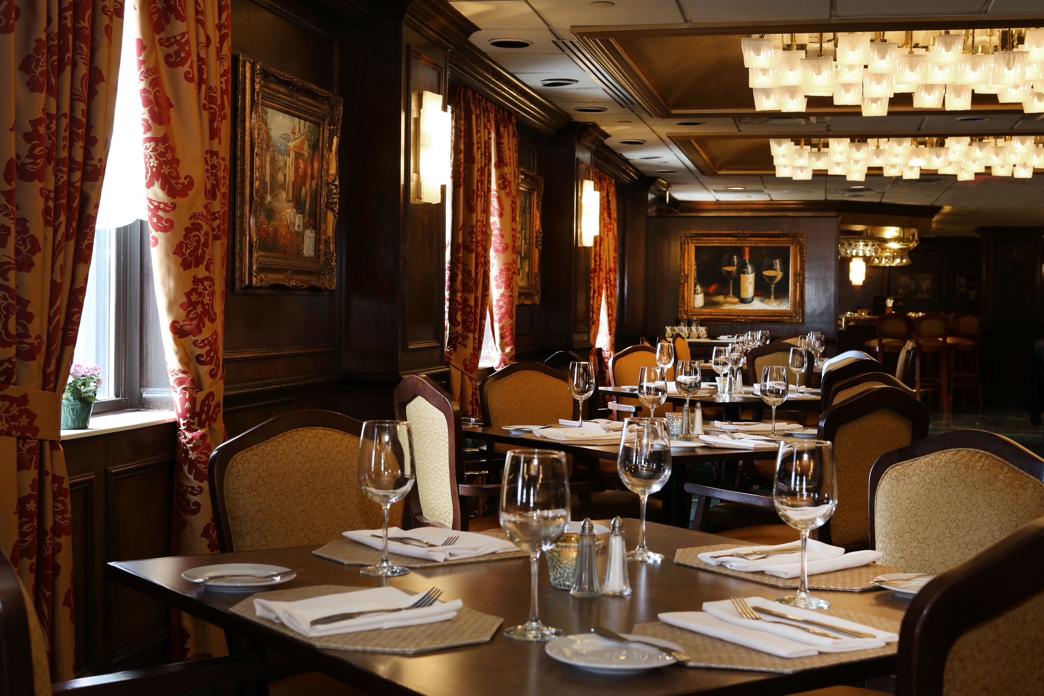 A restaurant with tables set for dining, featuring chandeliers and framed artwork on the walls.