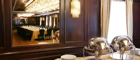 Une salle de banquet avec une longue table dressée pour un événement formel, un lustre et un buffet agrémenté de plats de service en argent.