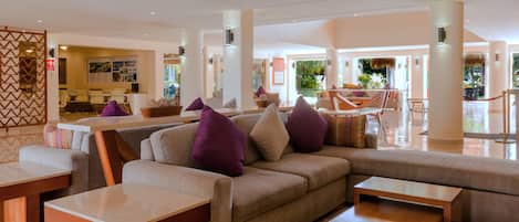 A spacious lobby with a large sofa, multiple tables, and a reception area.