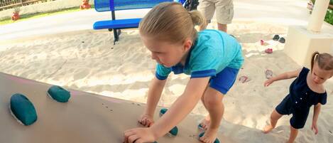 A child playing with large blue foam blocks on a sandy surface.