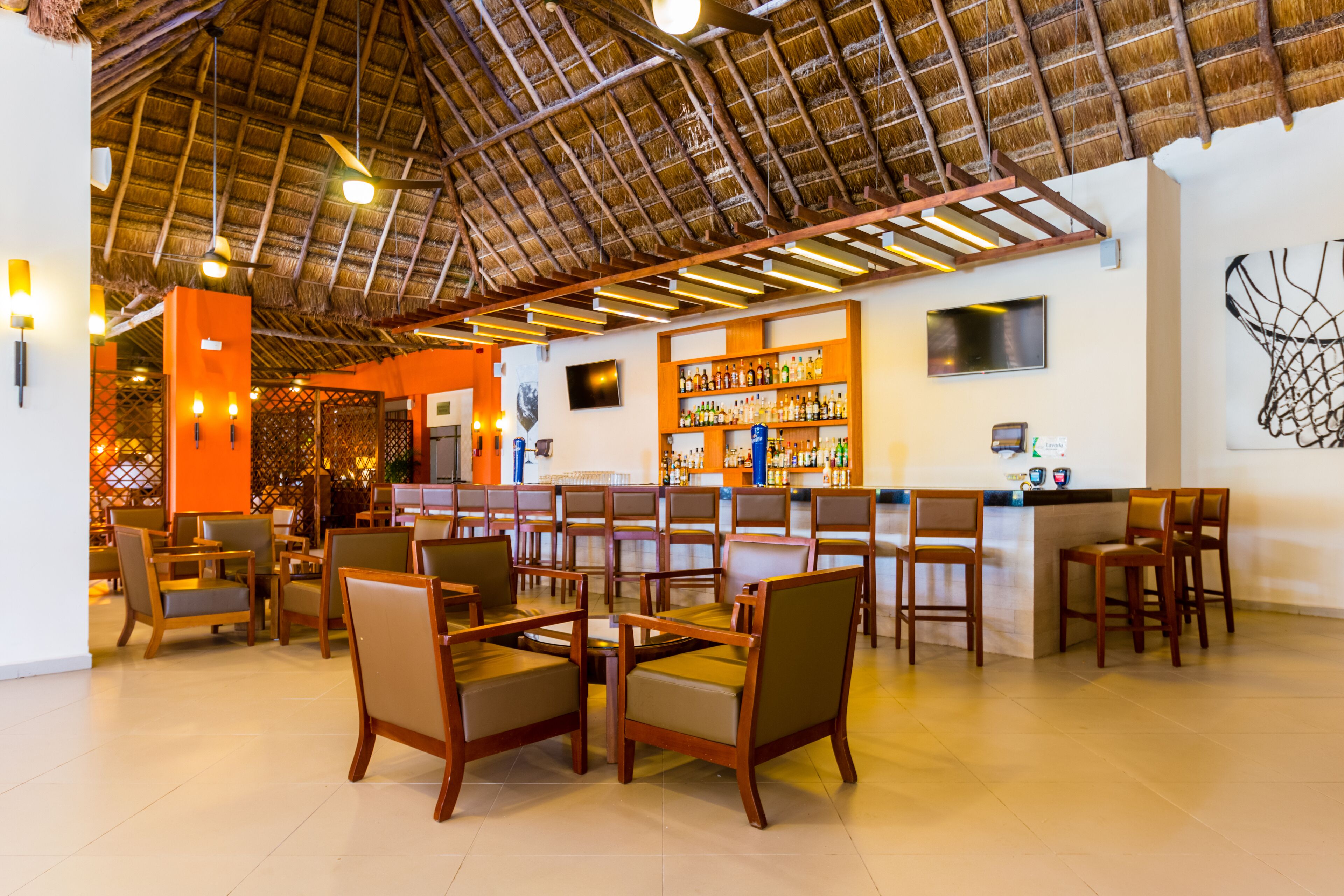 A restaurant with a thatched roof, wooden chairs, a bar area, and a wall-mounted TV.