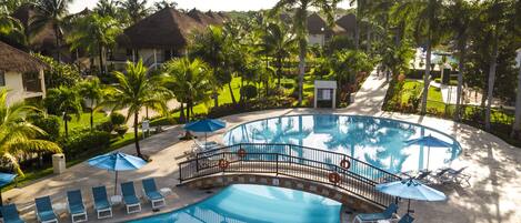 Área de piscina em resort, com ponte, espreguiçadeiras e palmeiras.