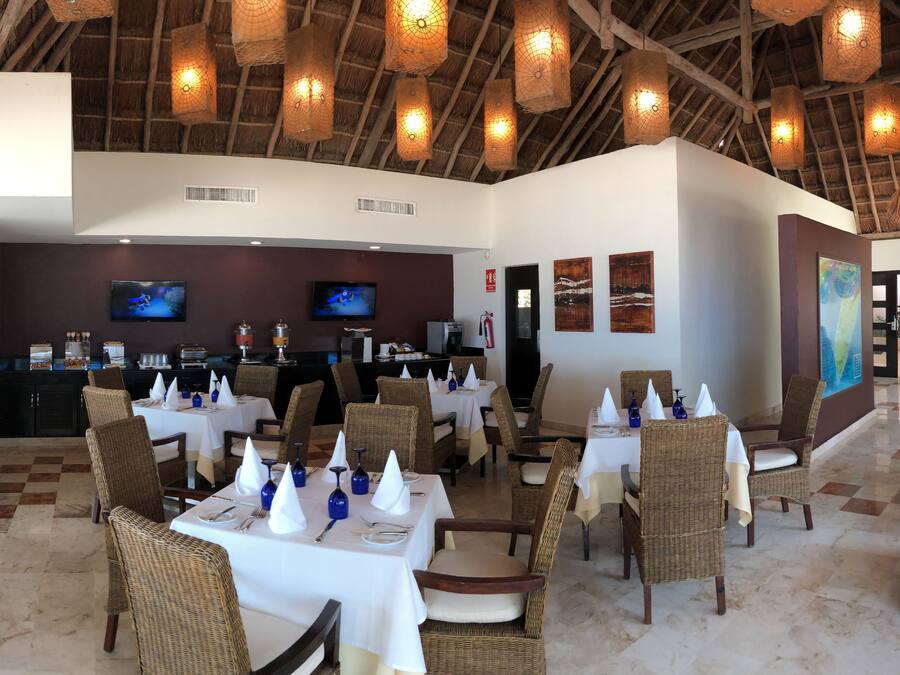 Un restaurante con mesas dispuestas para comer, sillas de mimbre y una pantalla de televisión en la pared.