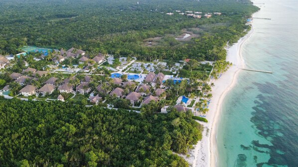 An aerial view of a resort with multiple bungalow-style accommodations, a central pool area, and a beach adjacent to the ocean.
