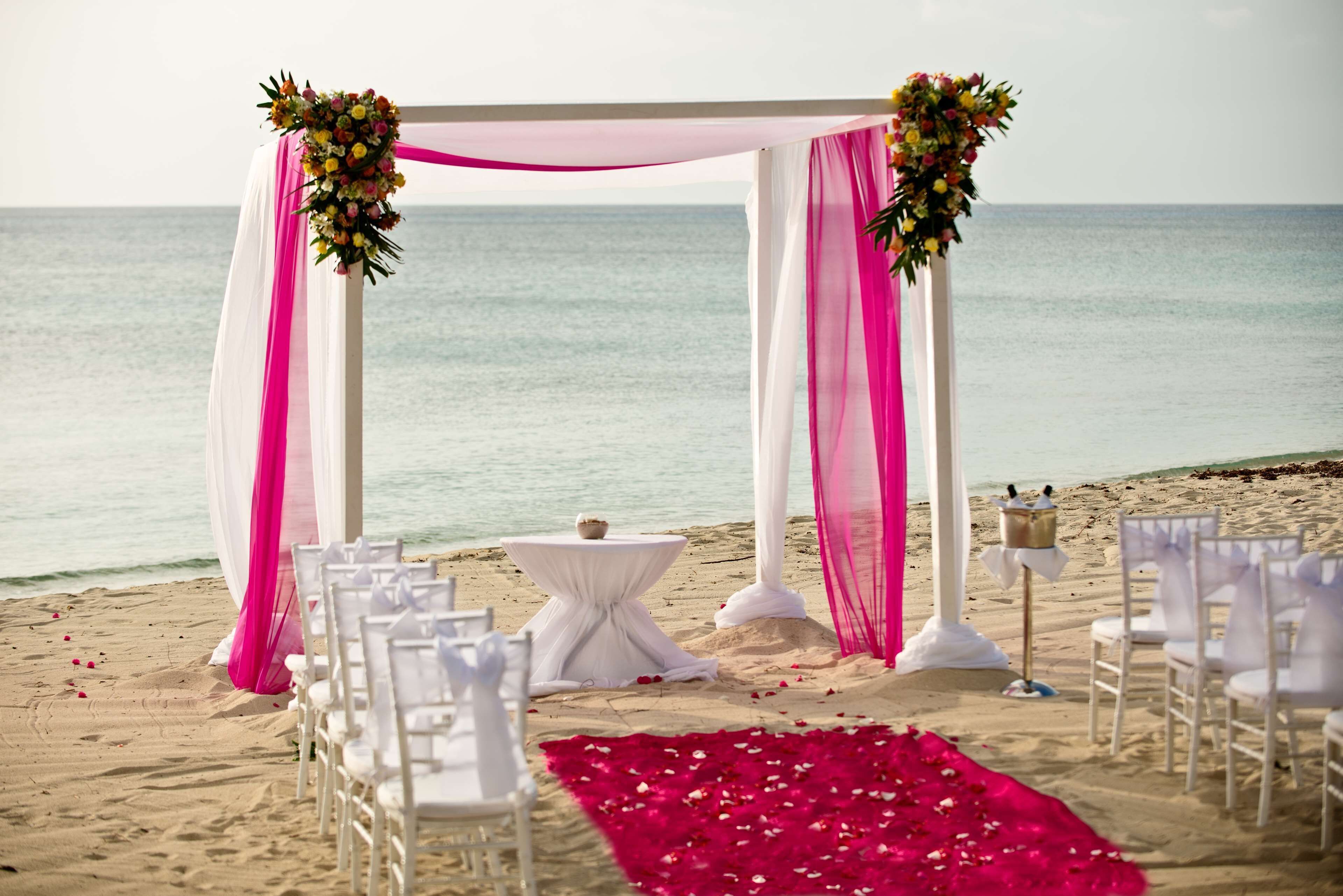 A beach wedding setup with a white arch, white chairs, and a table with a white tablecloth.