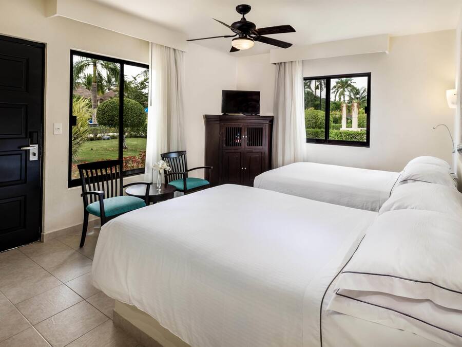 A hotel room with two beds, a ceiling fan, a TV on a cabinet, a chair, and a view of the outdoors.