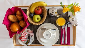 Bandeja de desayuno con cruasanes, una cesta de frutas, un vaso de zumo de naranja y un pequeño ramo de flores.