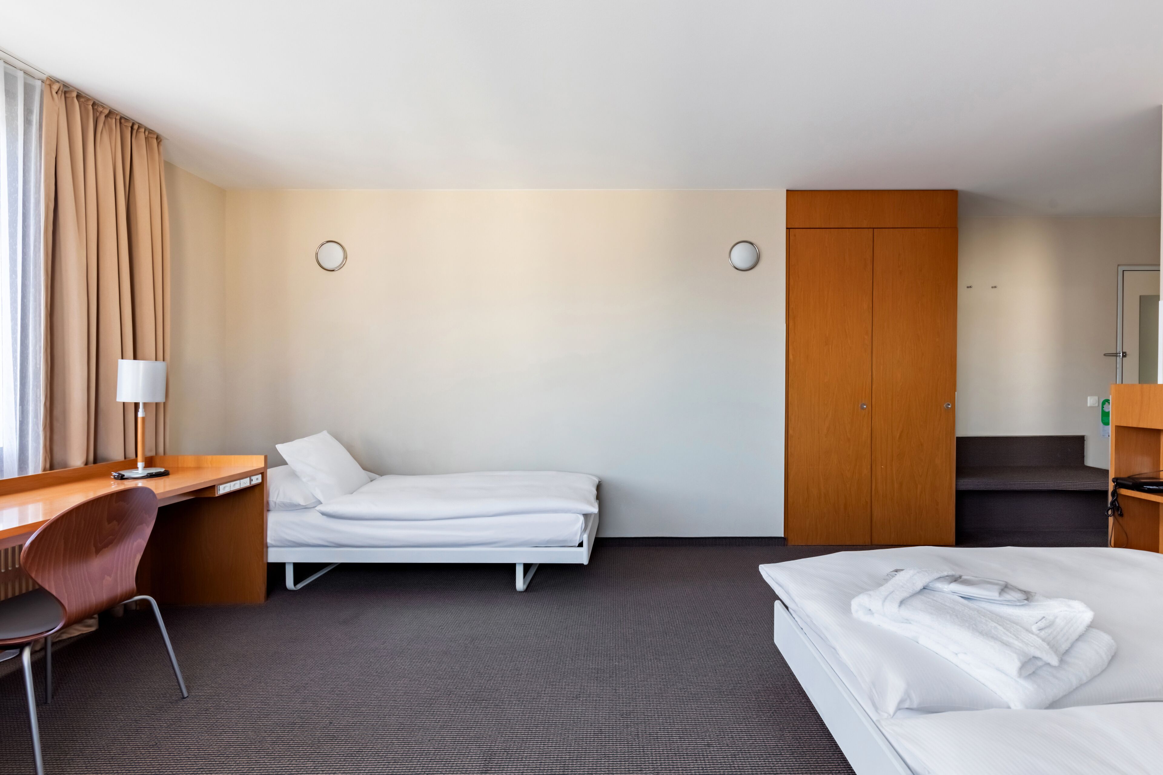 A hotel room with a bed, a desk, a chair, a wardrobe, and a bathroom.