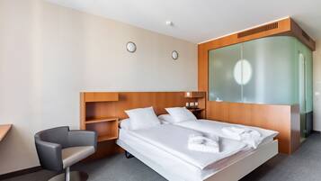 A modern hotel room with a large bed, a seating area, and a glass partition.