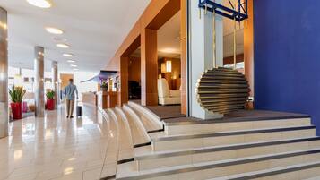 Un moderno vestíbulo de hotel con una escalera curva, una recepción y una gran columna decorativa.