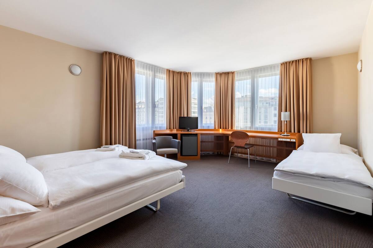 Una habitación de hotel con dos camas, un escritorio con computadora, una silla y un televisor.