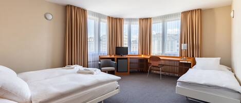 Une chambre d’hôtel avec deux lits, un bureau, une chaise, une télévision et de grandes fenêtres avec des rideaux.