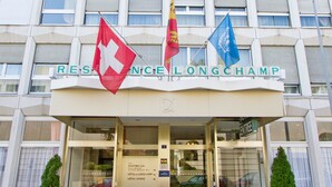 A hotel entrance with flags, signage, and a glass door. - Drake Longchamp (Geneva)