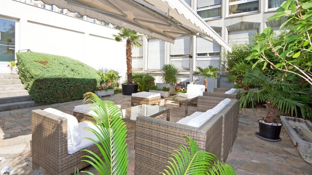 An outdoor patio with wicker furniture, potted plants, and a stone floor. - Drake Longchamp (Geneva)