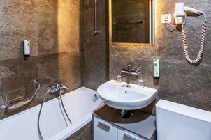 Un baño con bañera, lavamanos y secador de pelo fijado a la pared.