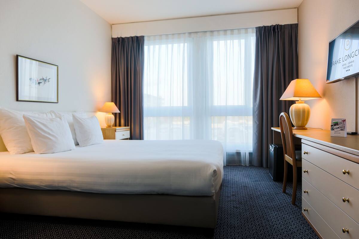 A hotel room with a large bed, two bedside tables with lamps, a desk with a chair, and a TV on the wall.