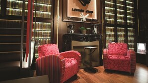 A lounge area with two red upholstered chairs, a fireplace, and bookshelves filled with books. - Drake Longchamp (Geneva)