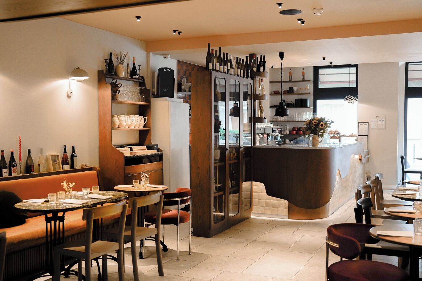 Un restaurant doté d’un bar, d’un espace pour s’asseoir et d’une variété de bouteilles de vin exposées sur des étagères.