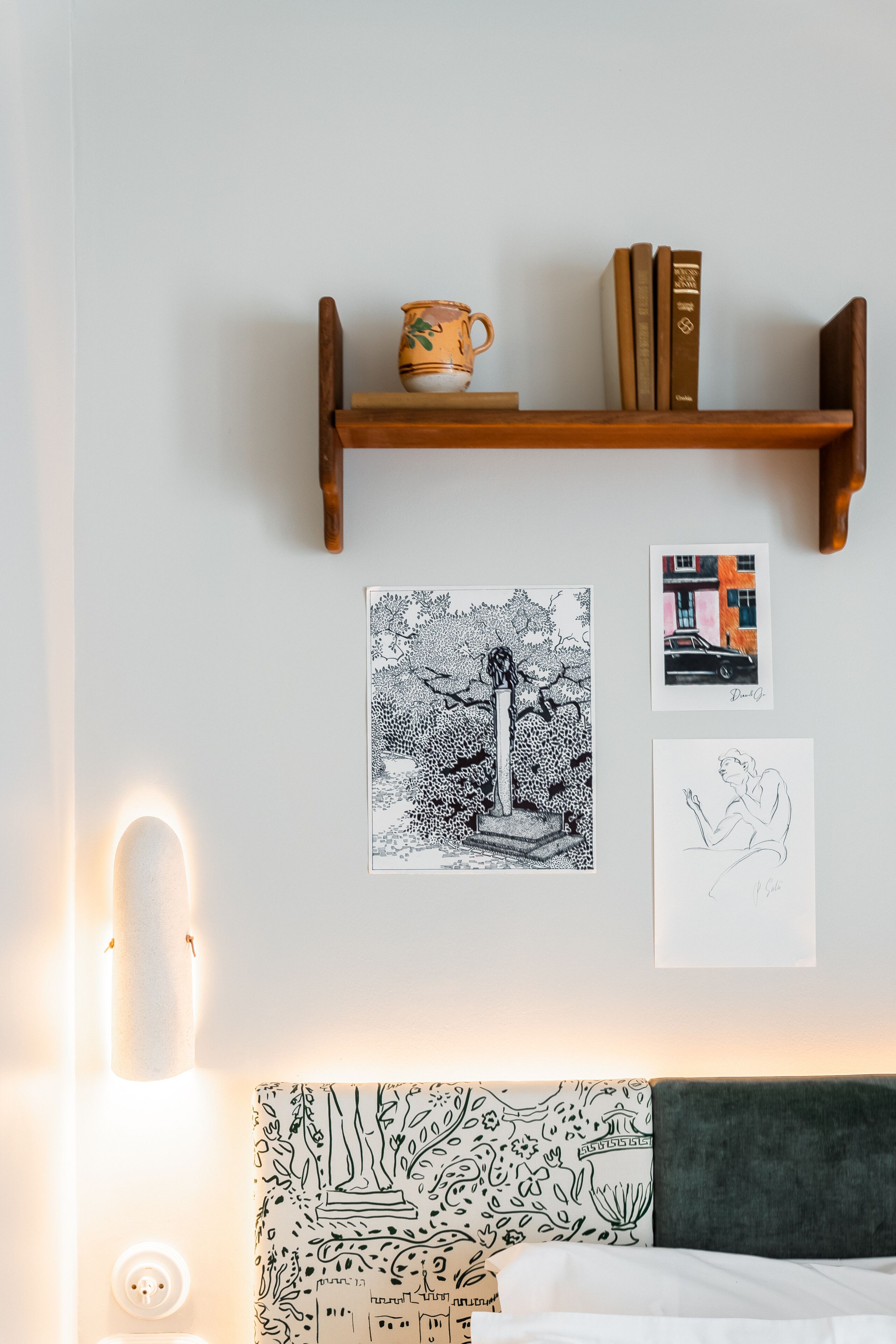 Un dormitorio con cama, una estantería en la pared con libros y una taza, y una obra de arte en la pared.