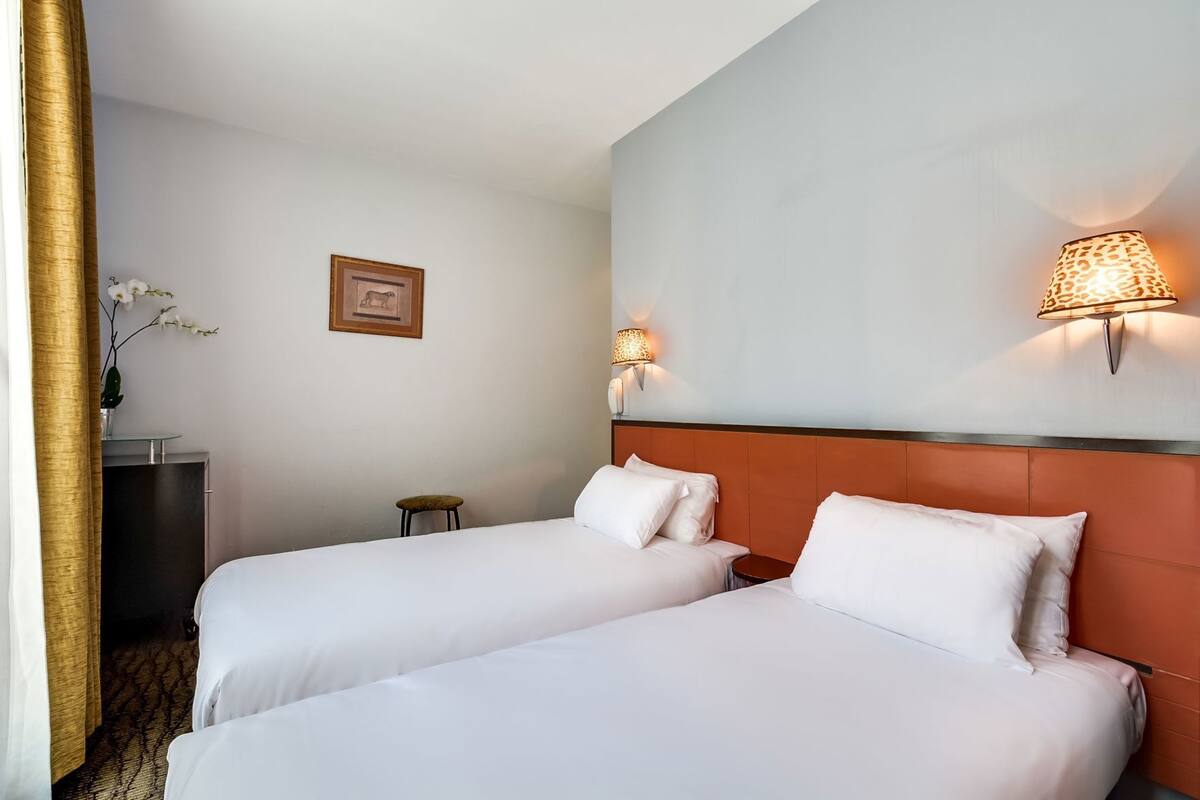 A hotel room with two beds, a desk, a chair, a lamp, and a framed picture on the wall.
