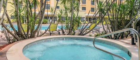 Un jacuzzi rodeado de palmeras y sillas de descanso, con una piscina al fondo.