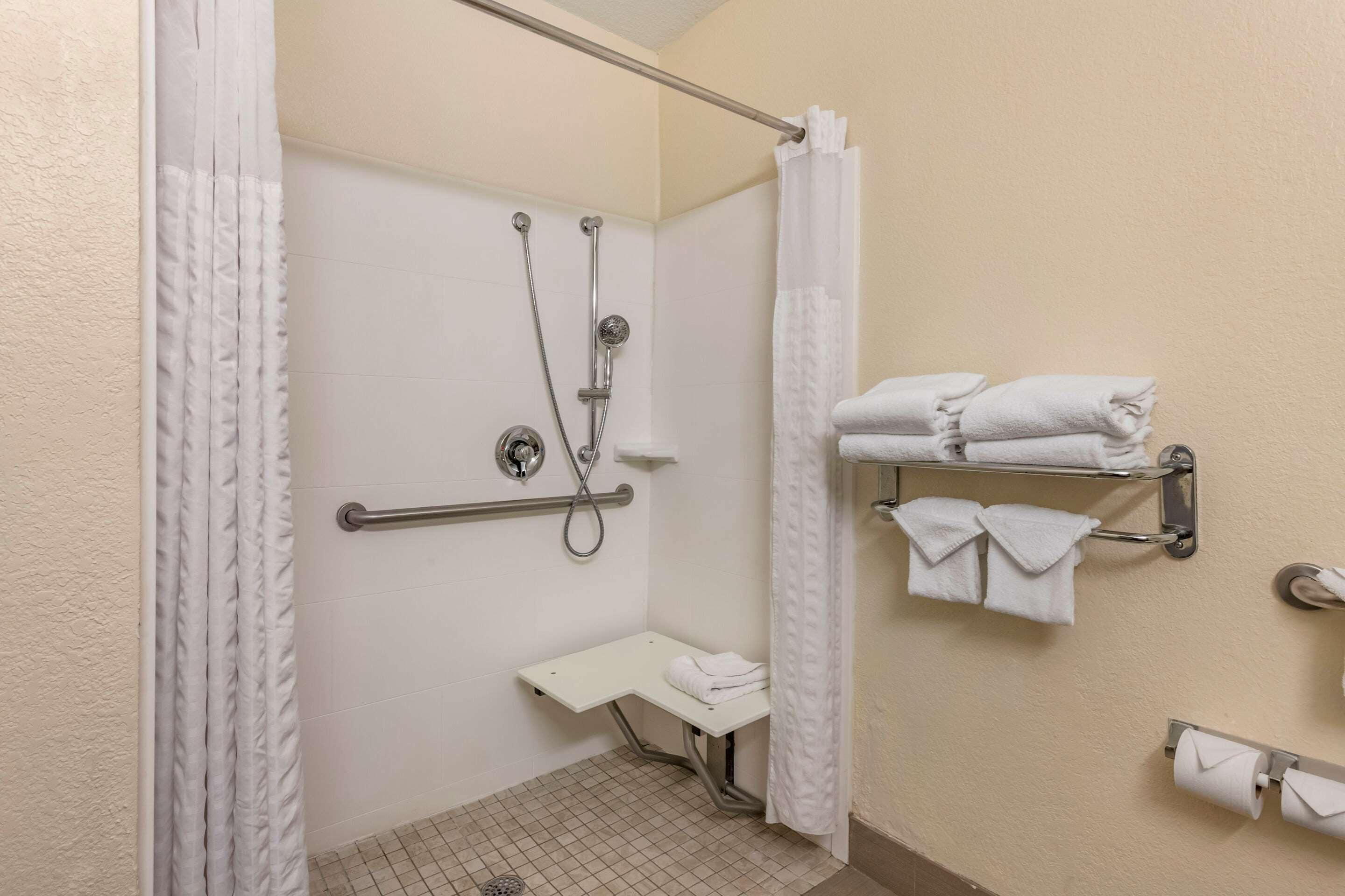 A bathroom with a shower, grab bars, a bench, and towel racks.