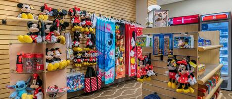 Una tienda con estantes llenos de peluches, incluyendo a Mickey Mouse y otros personajes, y una exhibición de cortinas con temática de Mickey Mouse.